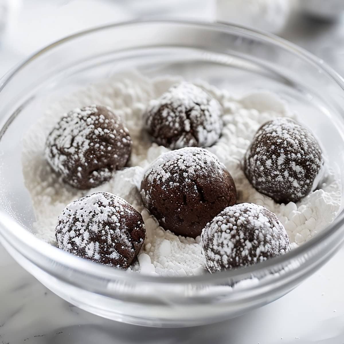 Close Up of Balls of Fudge Crinkle Cookie Dough in a Bowl of Powdered Sugar