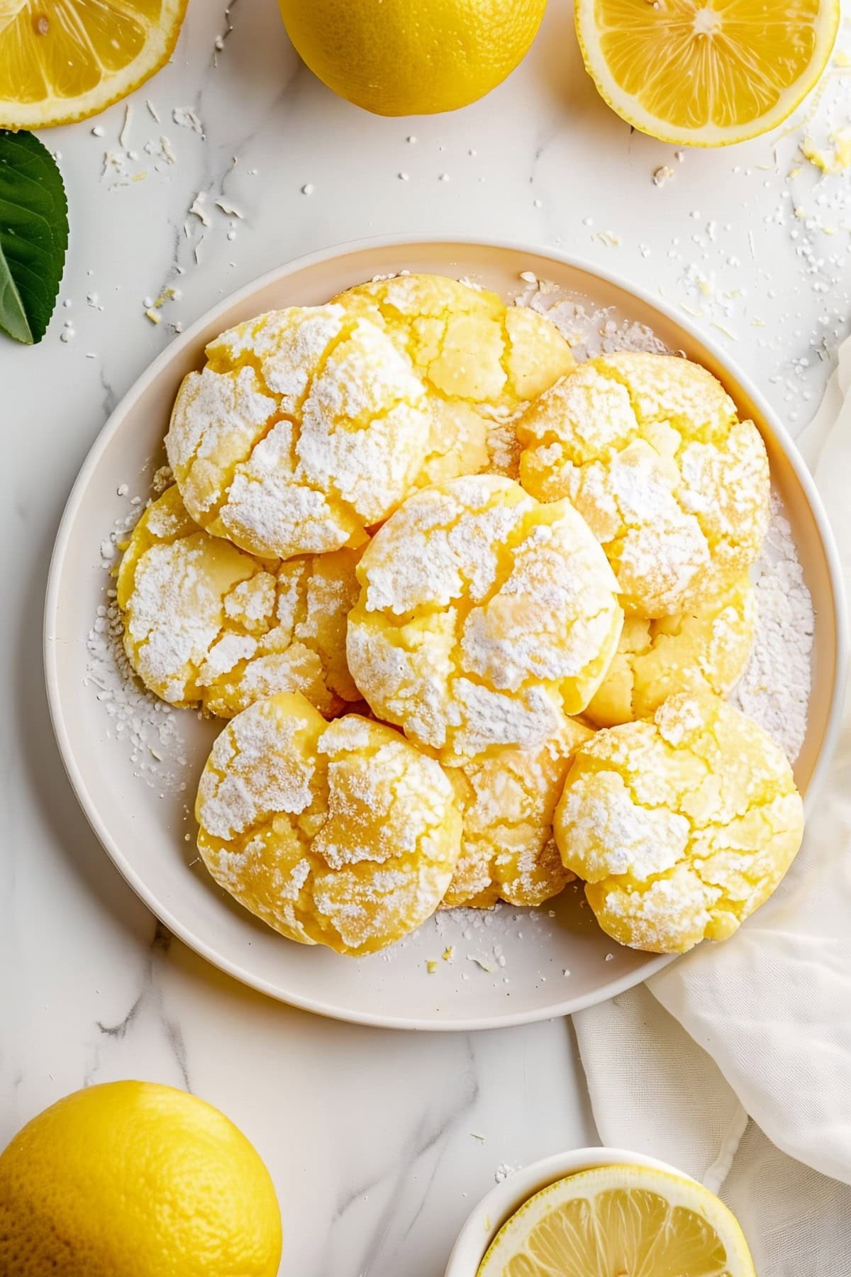 Top View of Lemon Crinkle Cookies on a White Plate on a White Marble Table with Lemons 