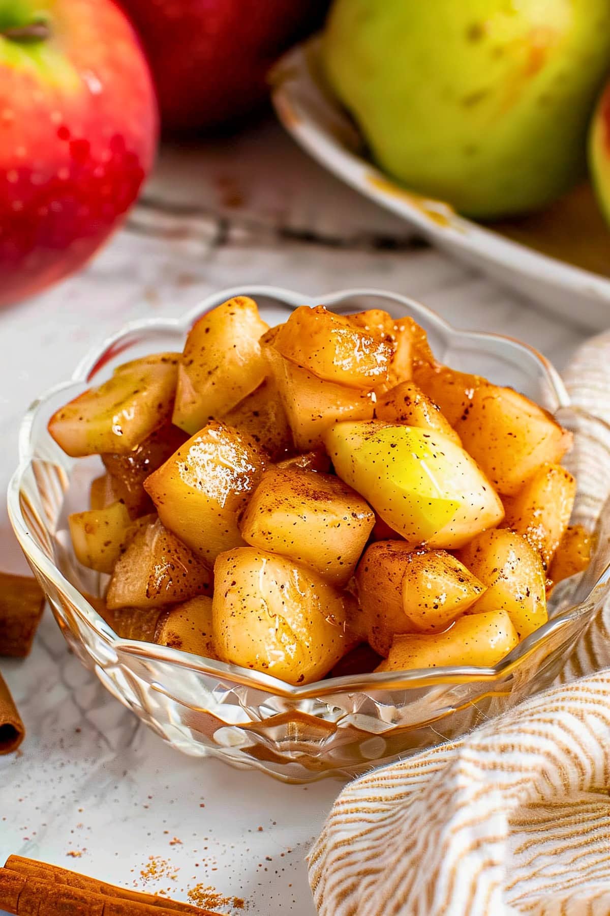 Close Up of Cinnamon-Spiced Microwave Baked Apples in a Glass Dish on a Table with Fresh Apples and Cinnamon Sticks in the Background
