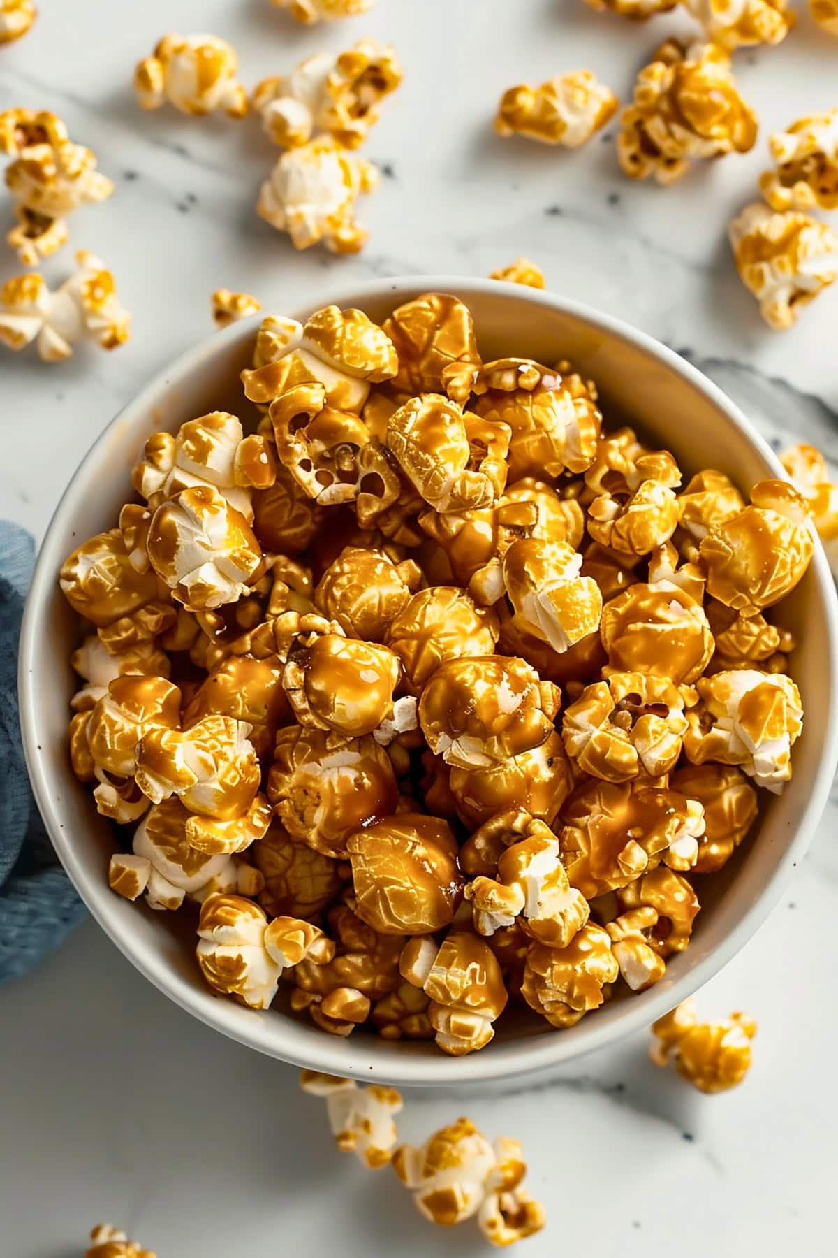 Top View Microwave Caramel Popcorn in a Bowl on a White Marble Table with a Kitchen Towel