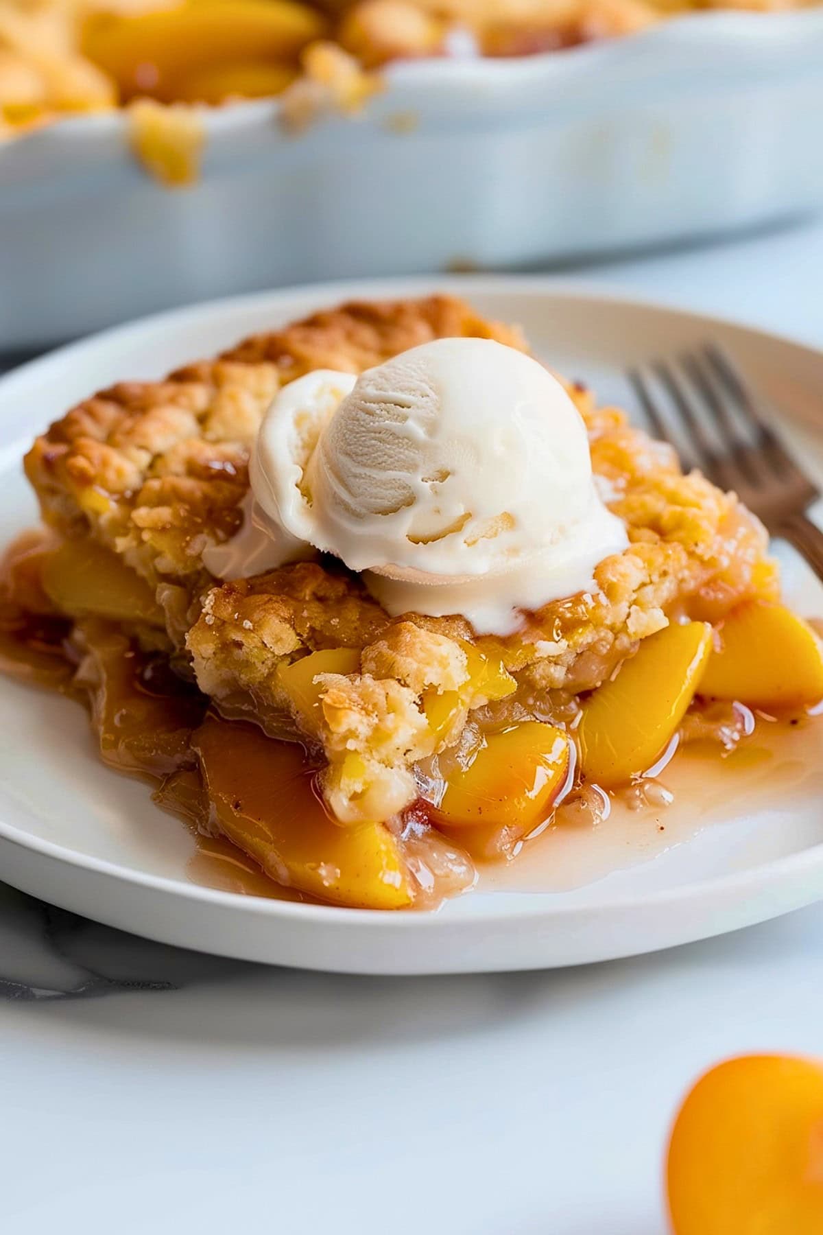 Slice of Peach Cobbler with Cake Mix on a Plate with Vanilla Ice Cream and a Fork