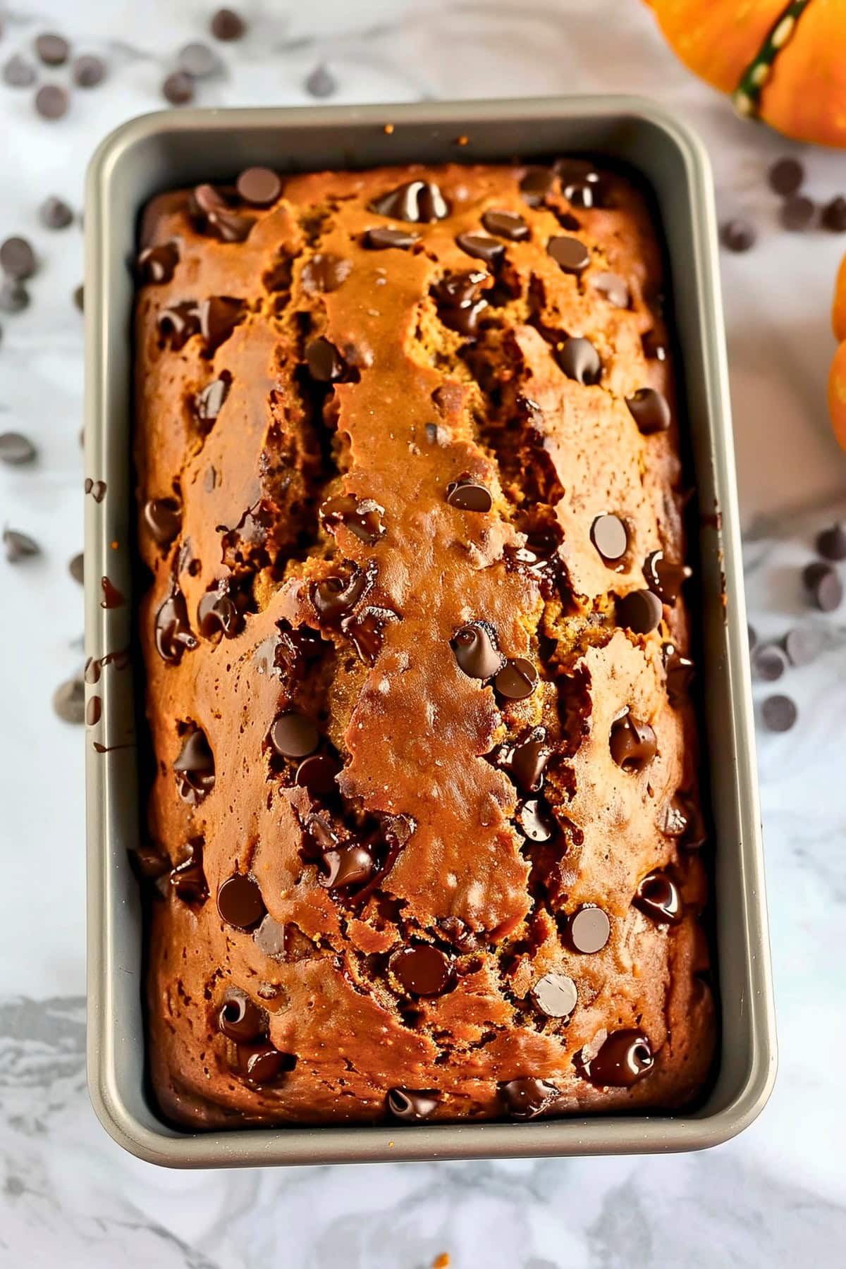 Top View Baked Pumpkin Chocolate Chip Bread Still in the Loaf Pan on a White Marble Table