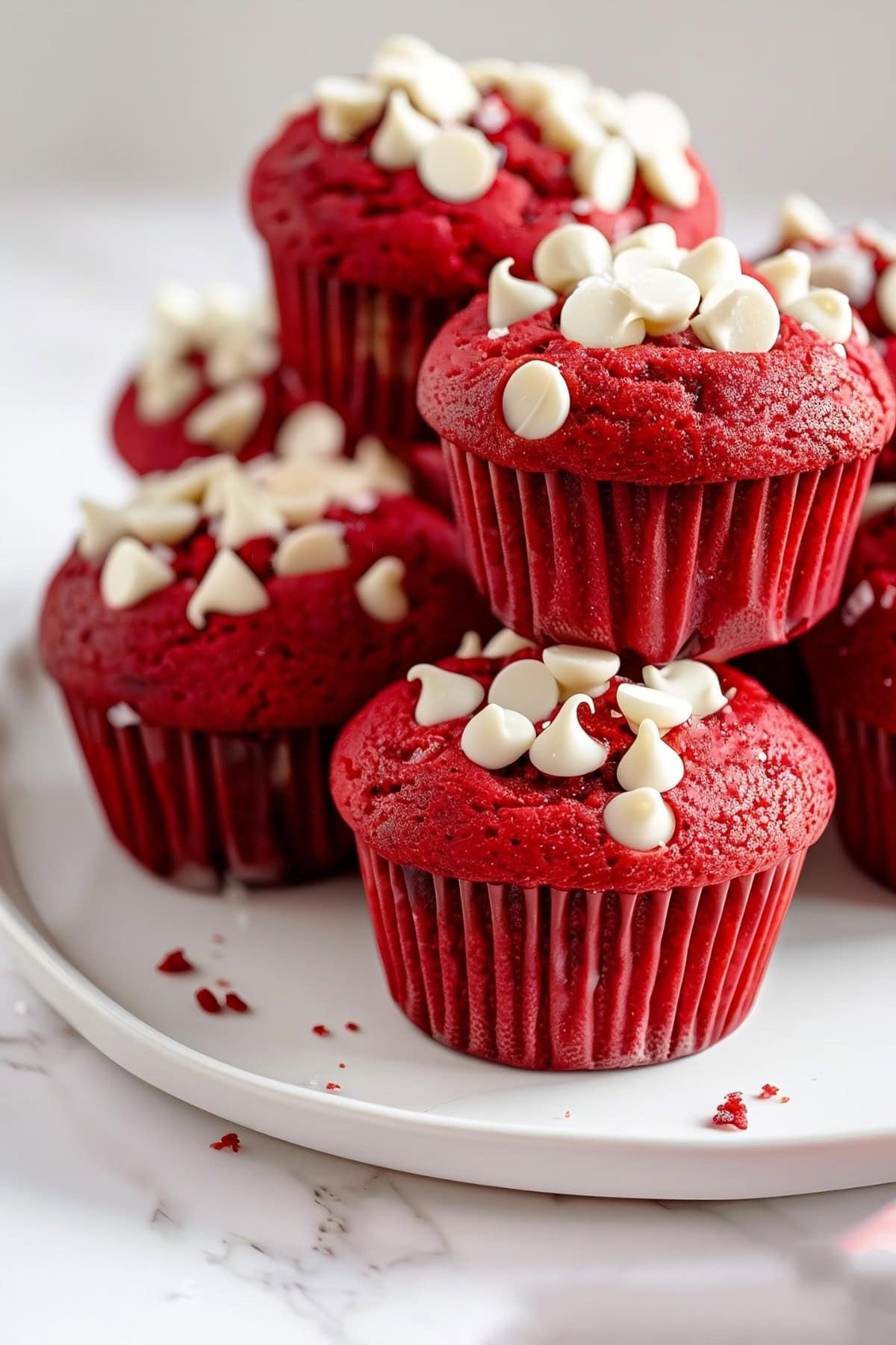Bunch of red velvet muffins with white mini chocolate chips served on a white plate.