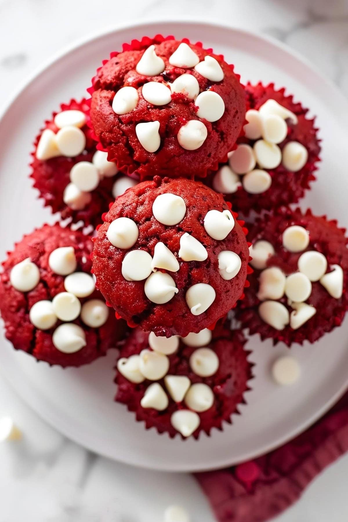 Top view of red velvet muffins with white chocolate chips arranged on a white plate.