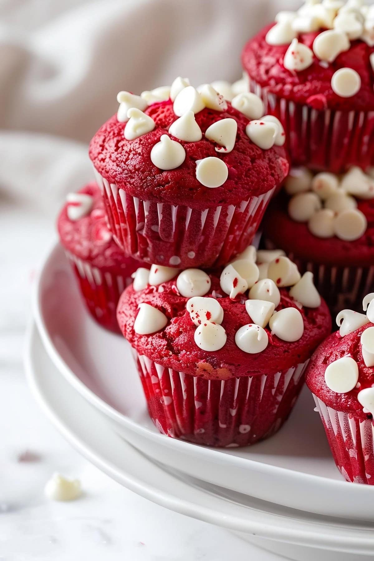 Red velvet muffins with white chocolate chips stacked on a white plate
