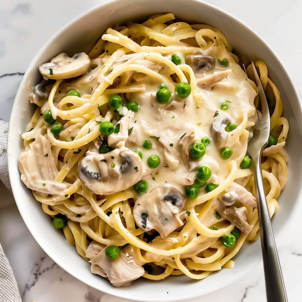 A bowl filled with turkey tetrazzini spaghetti, green peas and creamy mushroom soup.