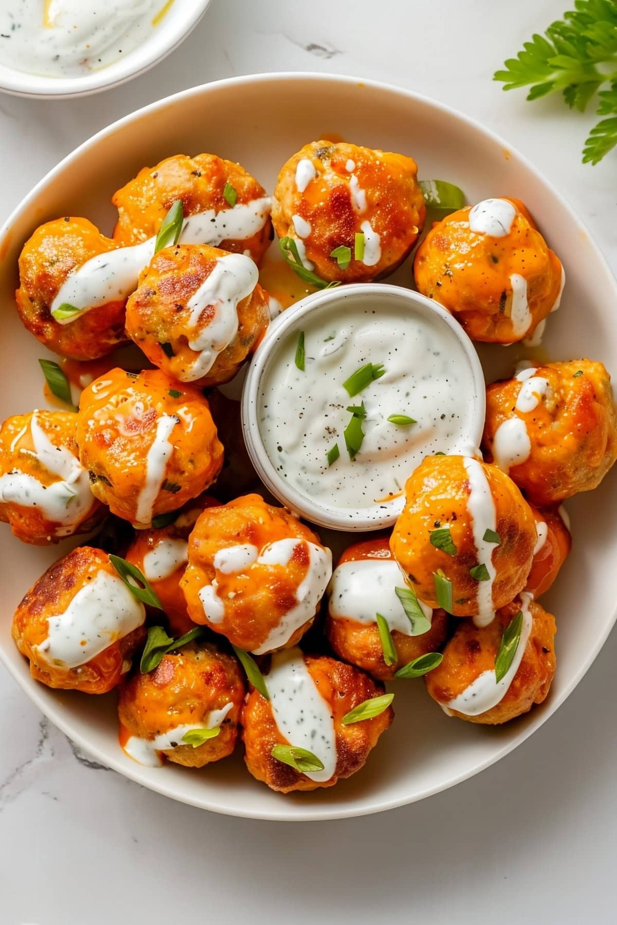 Buffalo chicken meatballs drizzled with bleu cheese yogurt dip, sprinkled with chopped chives, top down view