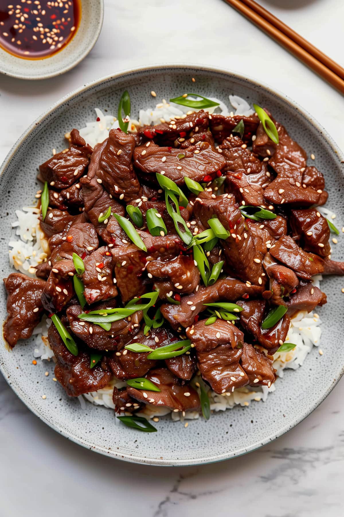 Homemade Mongolian beef with green onions, sesame seeds and red pepper flakes, served on a bed of rice