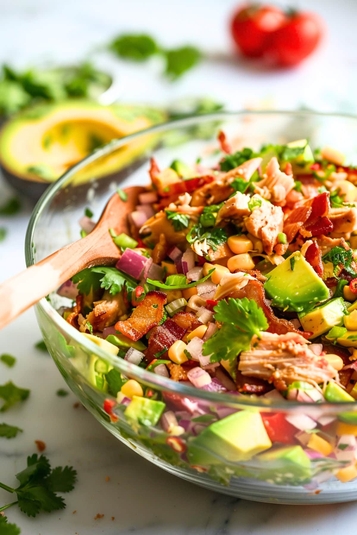 Mix of bacon, cooked and crumbled, shredded chicken breasts, small square slice ripe avocados, corn kernels, finely chopped small red onion, fresh cilantro chopped with olive oil and lime juice dressing served in a glass bowl,