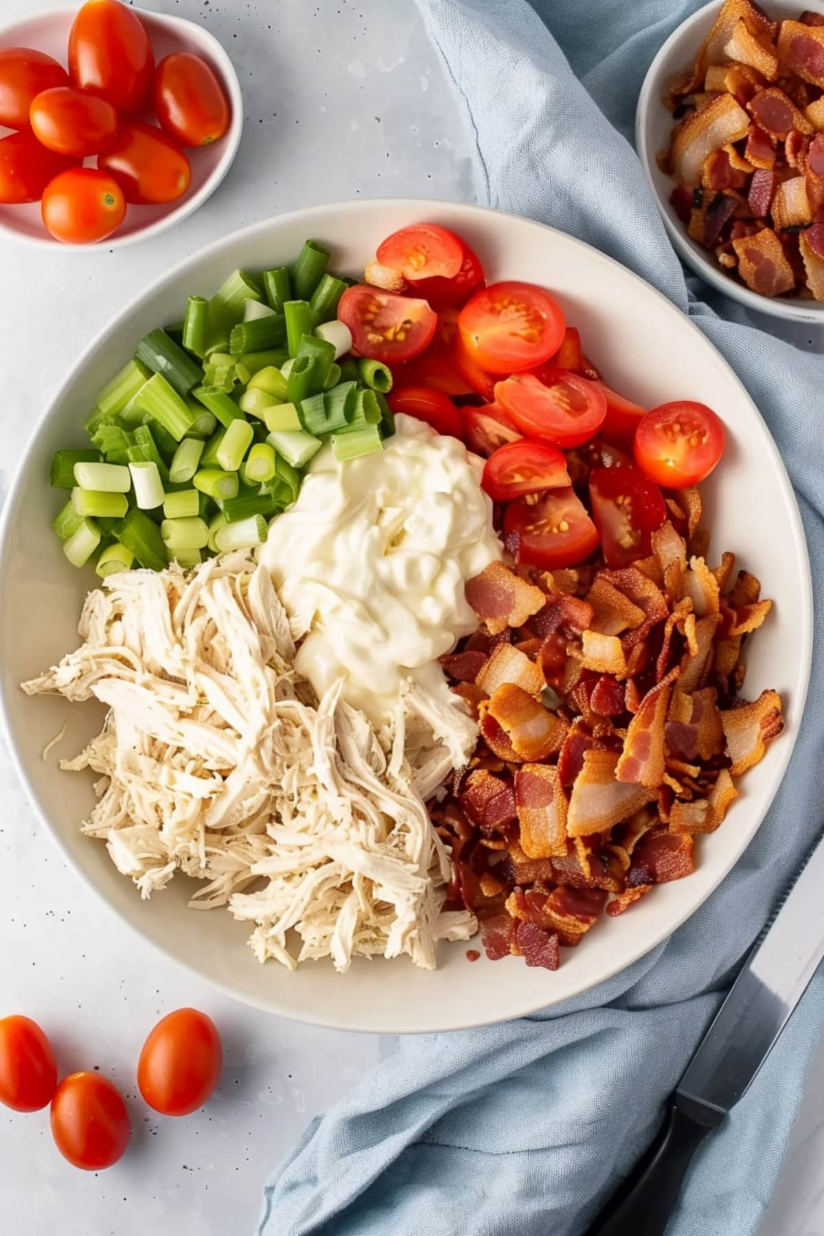 Shredded chicken, mayonnaise, chopped tomatoes, bacon and scallions in a white bowl, top view.