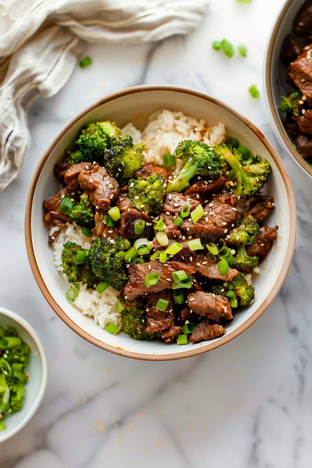 A bowl filled with beef and broccoli, sprinkled with green onions and sesame seeds.