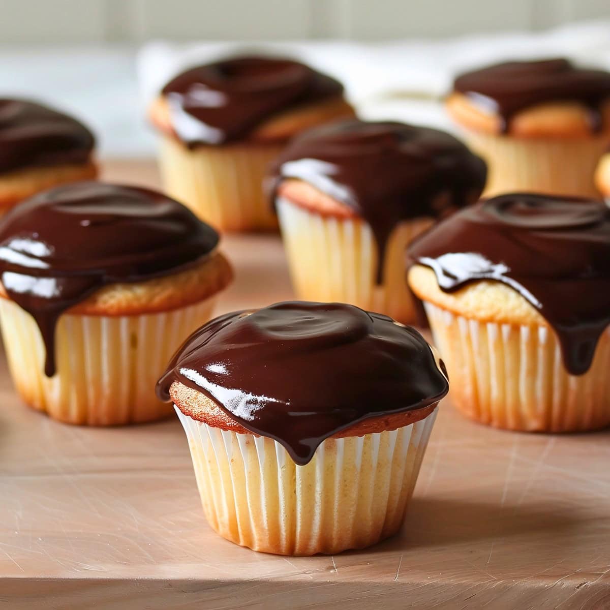 Bunch of Boston Cream Pie Cupcakes covered with chocolate ganache in a wooden board.