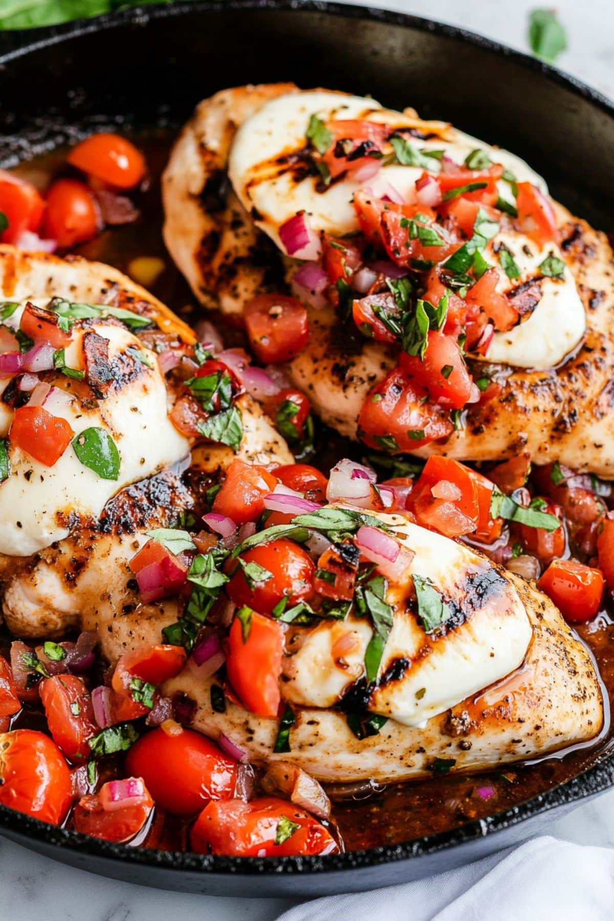 Chicken breast with melted mozzarella cheese, diced tomatoes and basil mixture on top cooked in a cast iron skillet.
