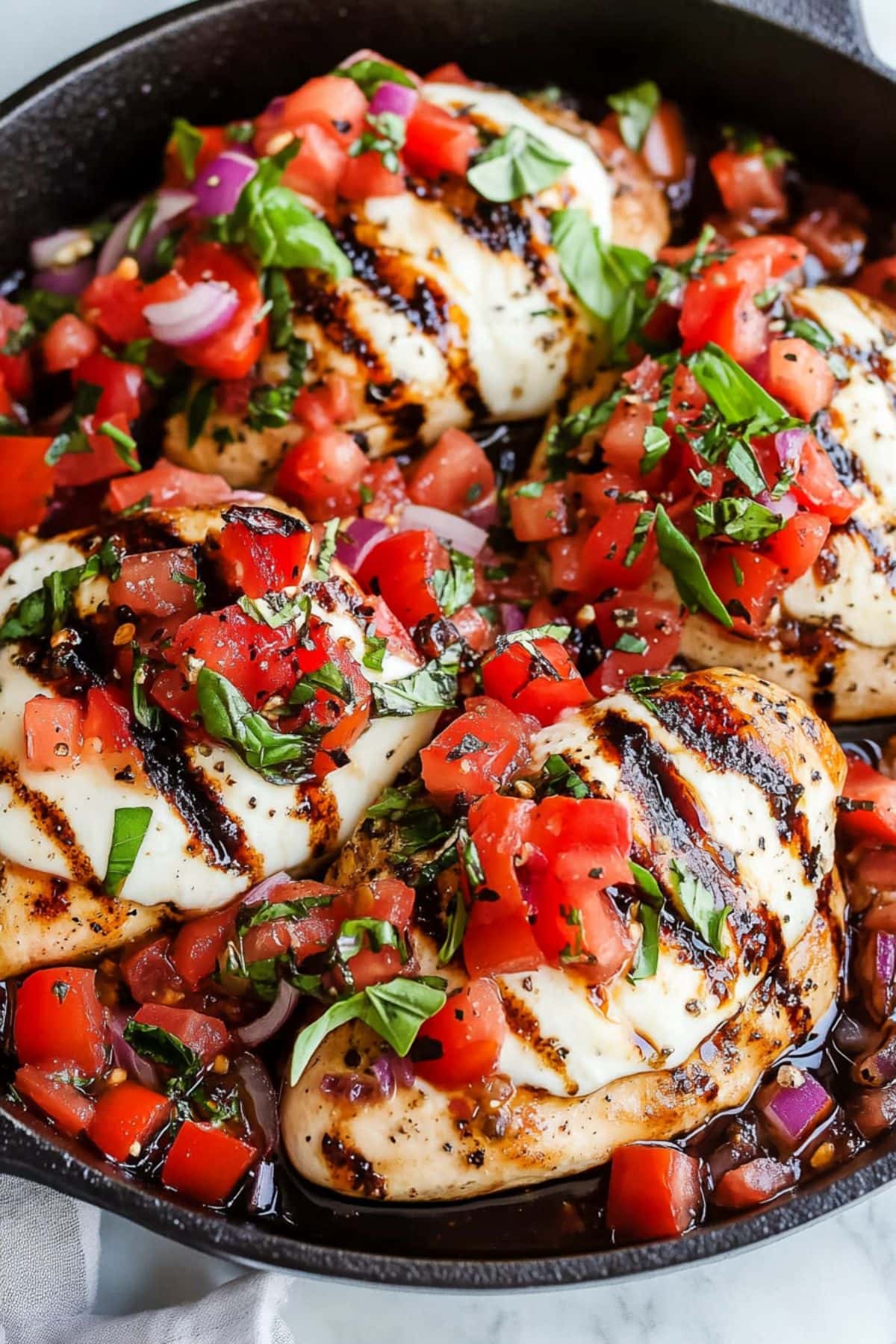 Chicken breasts topped with melty mozzarella and a vibrant tomato-basil mixture cooked in a cast iron skillet.