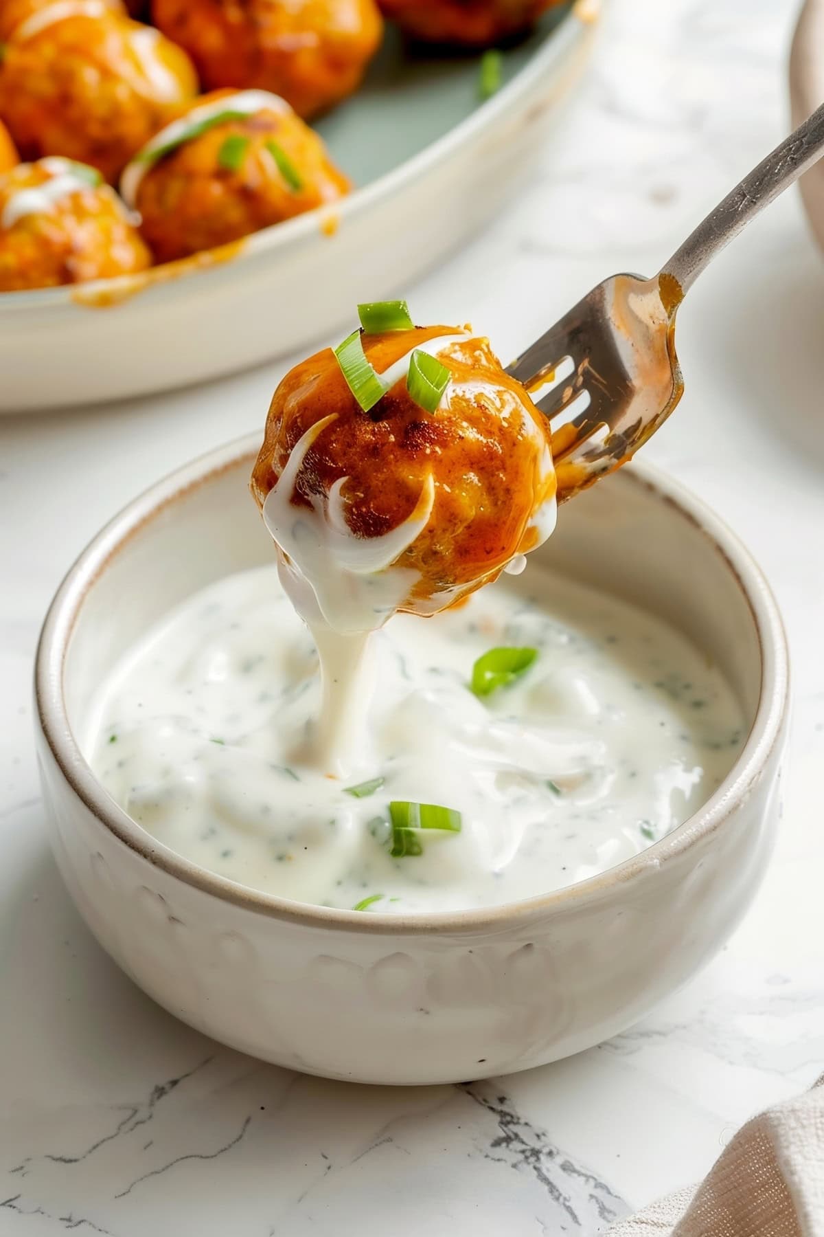 A buffalo chicken meatball on a fork being dipping into creamy dip.