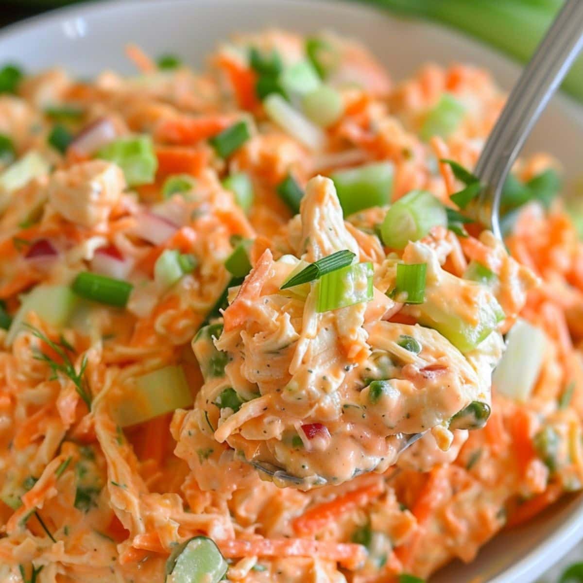 Spoonful scoop of buffalo chicken salad from a white bowl.