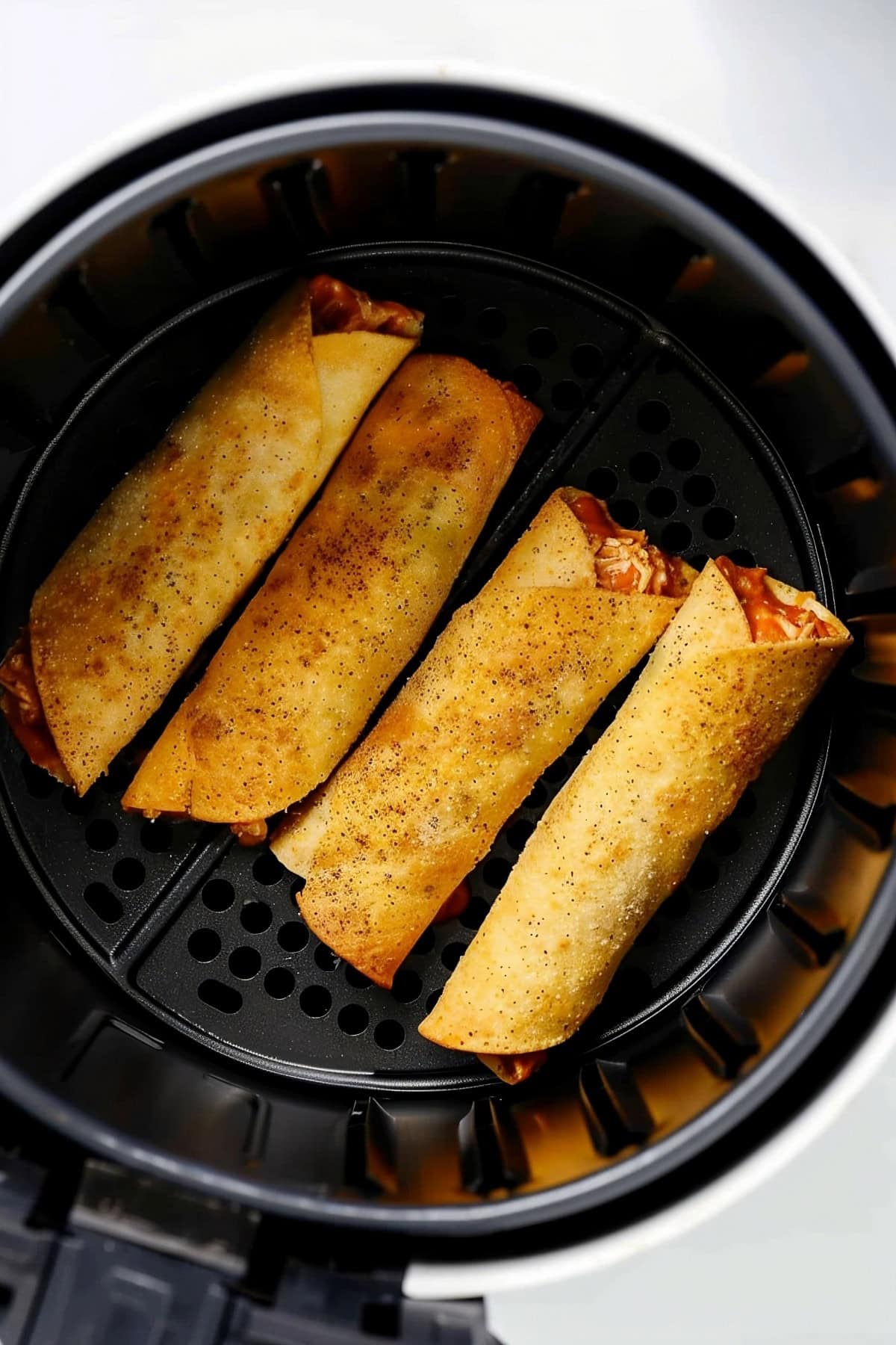 An air fryer filled with buffalo chicken taquitos.