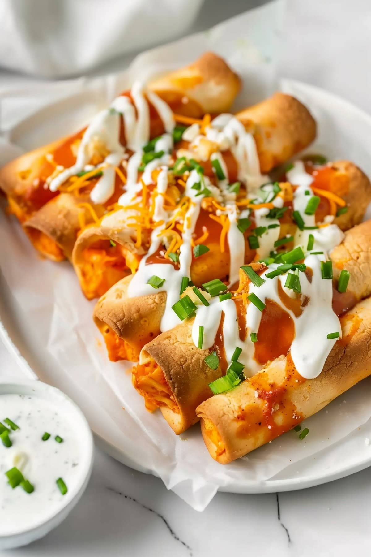 Spicy buffalo chicken taquitos drizzled with buffalo sauce and ranch dressing with chopped chives for garnish