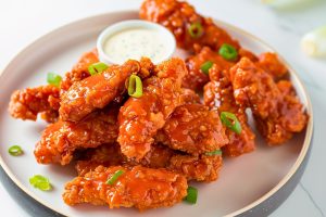 Bunch of buffalo sauce coated chicken tenders served in a plate with ranch dip.