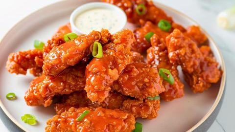 Bunch of buffalo sauce coated chicken tenders served in a plate with ranch dip.