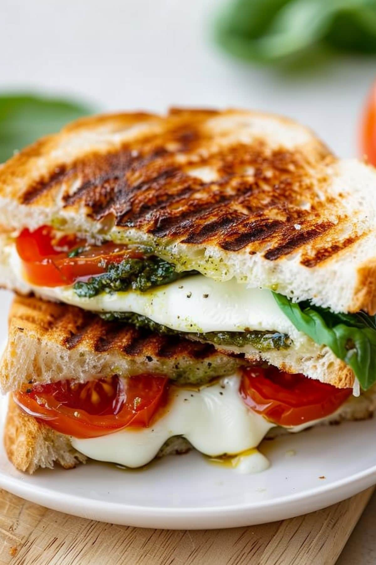 Sliced in half caprese grilled cheese sandwich served on a white plate.