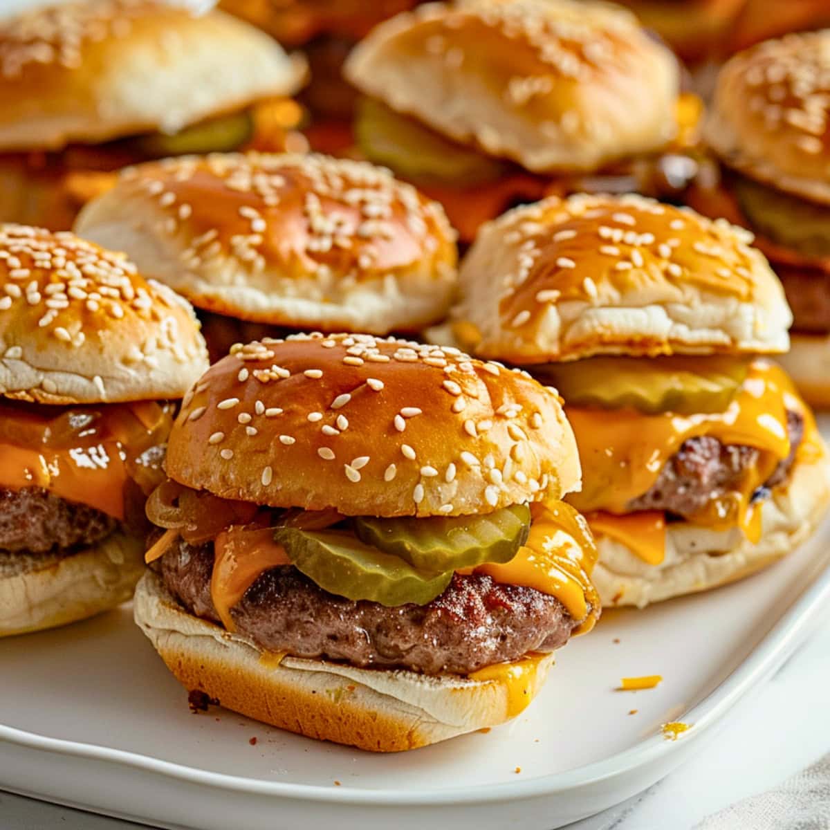 Cheeseburgers sliders with melted cheddar cheese, beef patty and sliced pickles.