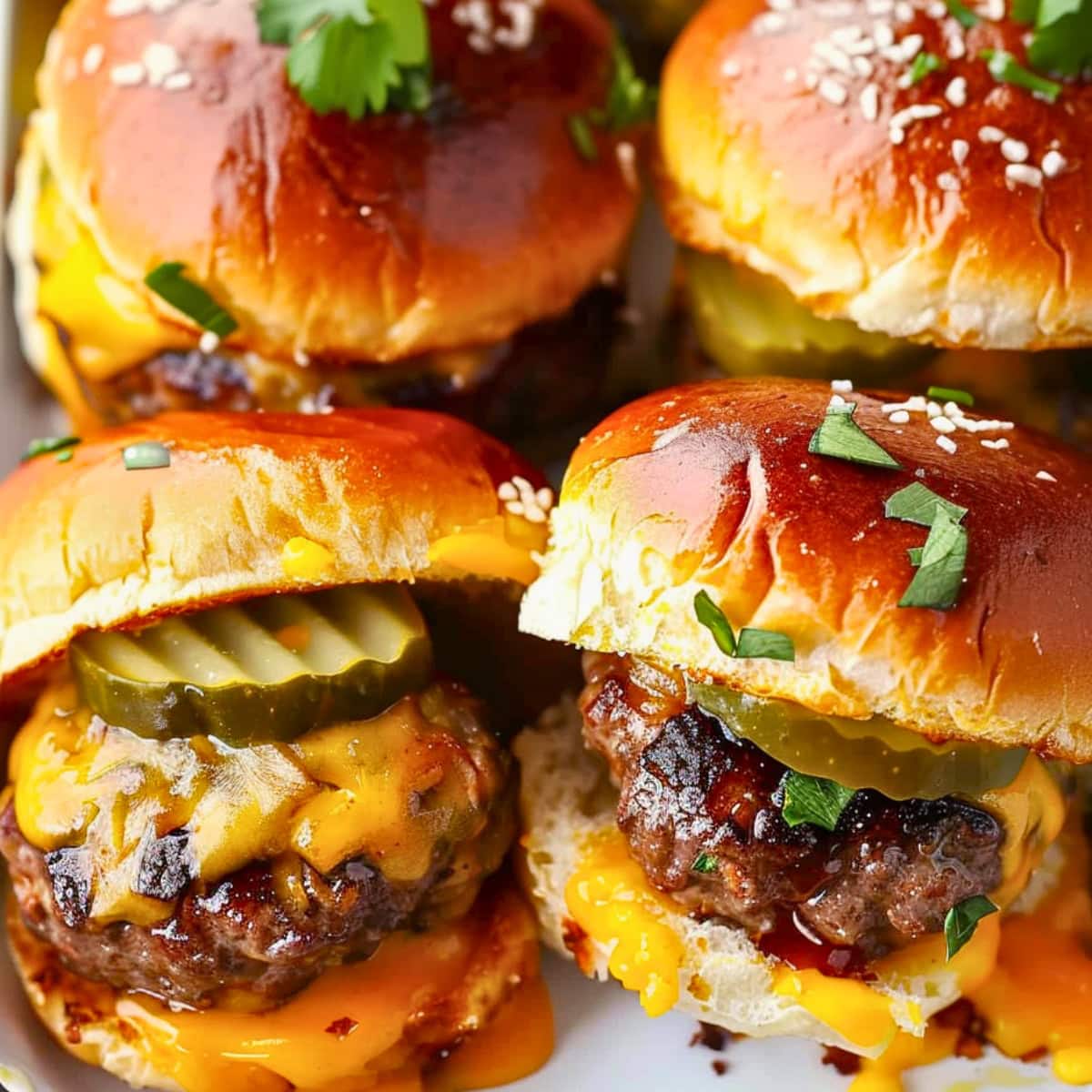 Bunch of cheesy cheese burger slides with melted cheese and pickles.