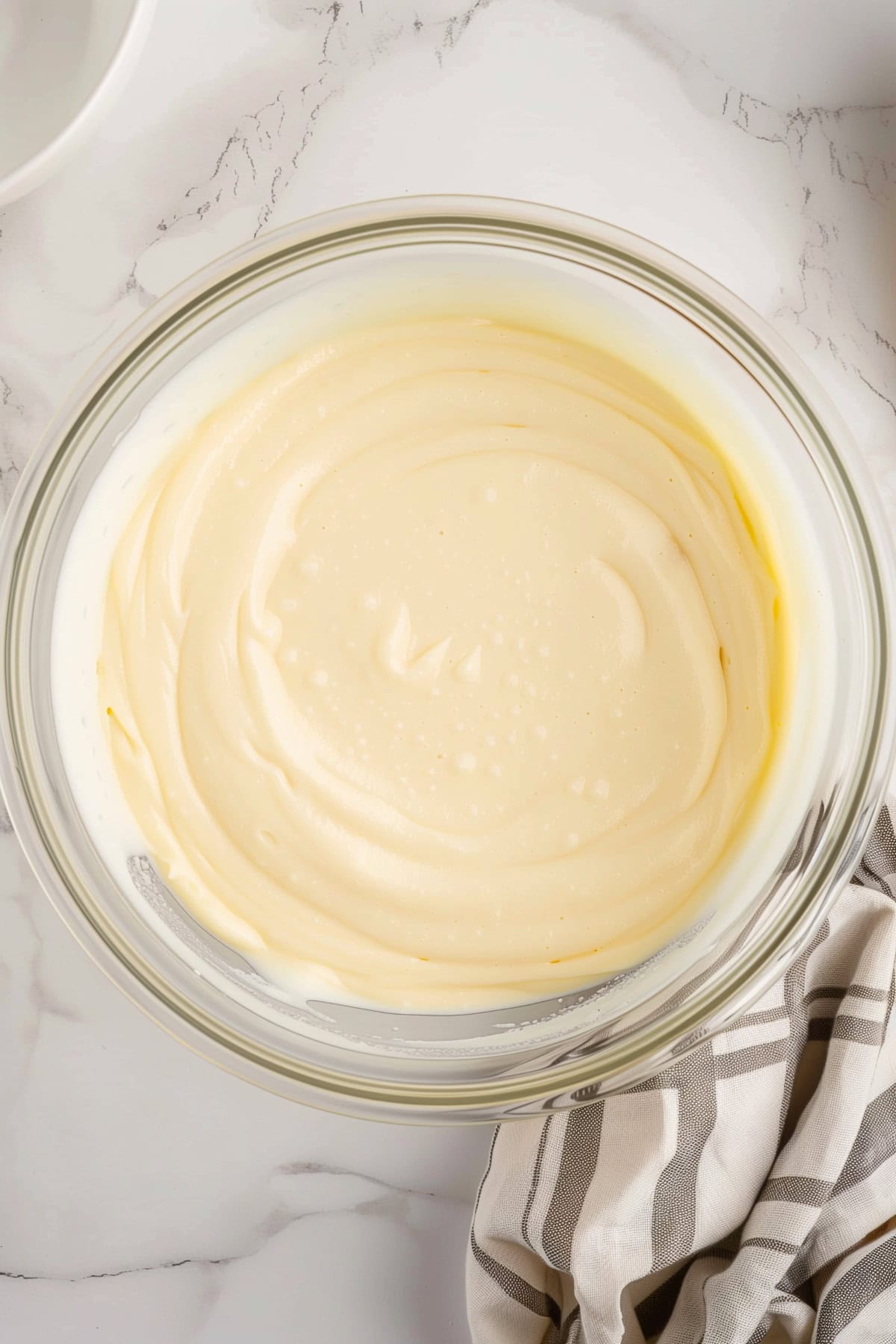 A glass bowl filled with cheesecake filling, top view.