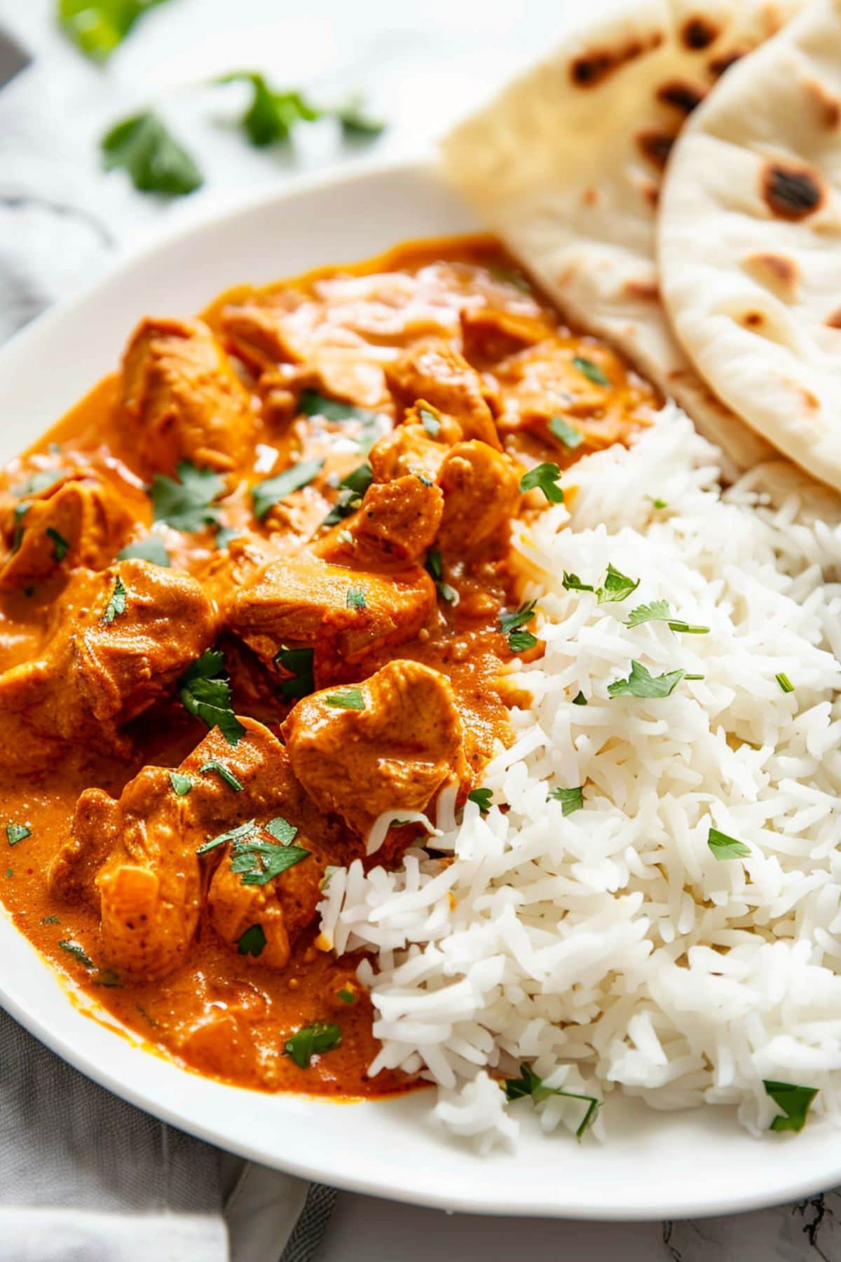 Homemade chicken tikka masala served with white rice and pita bread on a white plate.