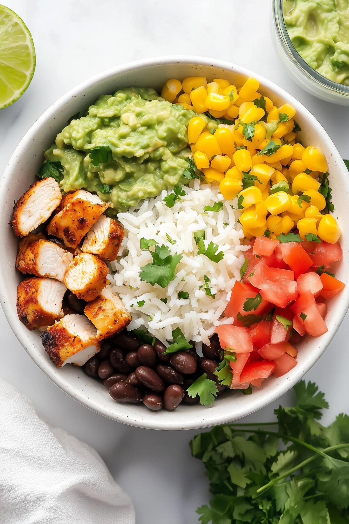 A Chipotle burrito bowl with cilantro lime rice, guacamole, corn, salsa, black beans and chicken, top view.