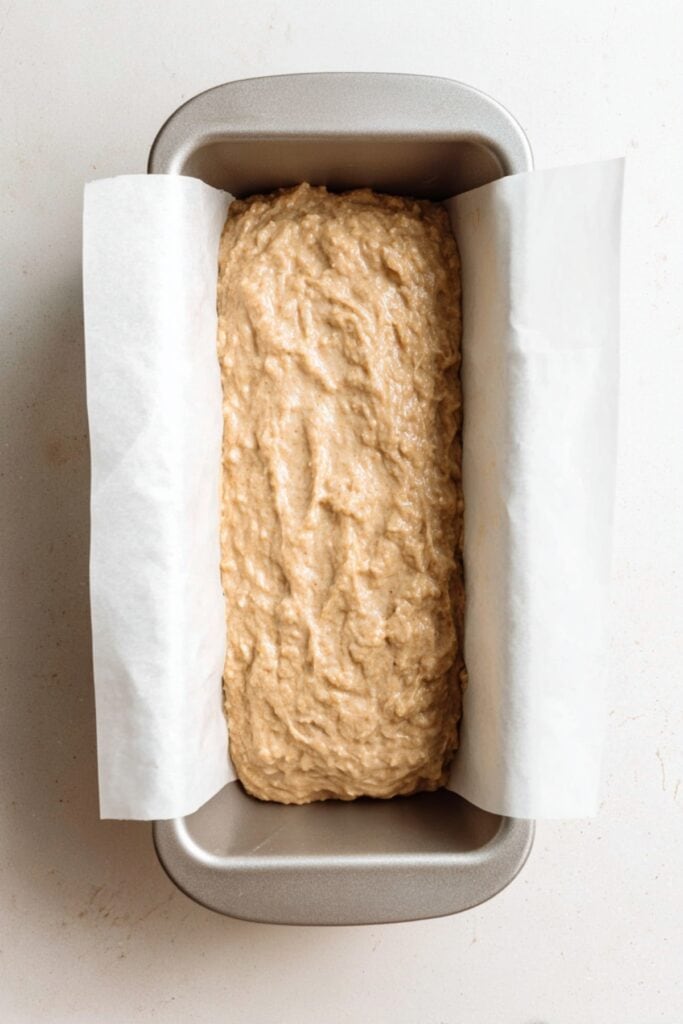 Banana bread batter poured into a parchment-lined loaf pan, ready to be baked.