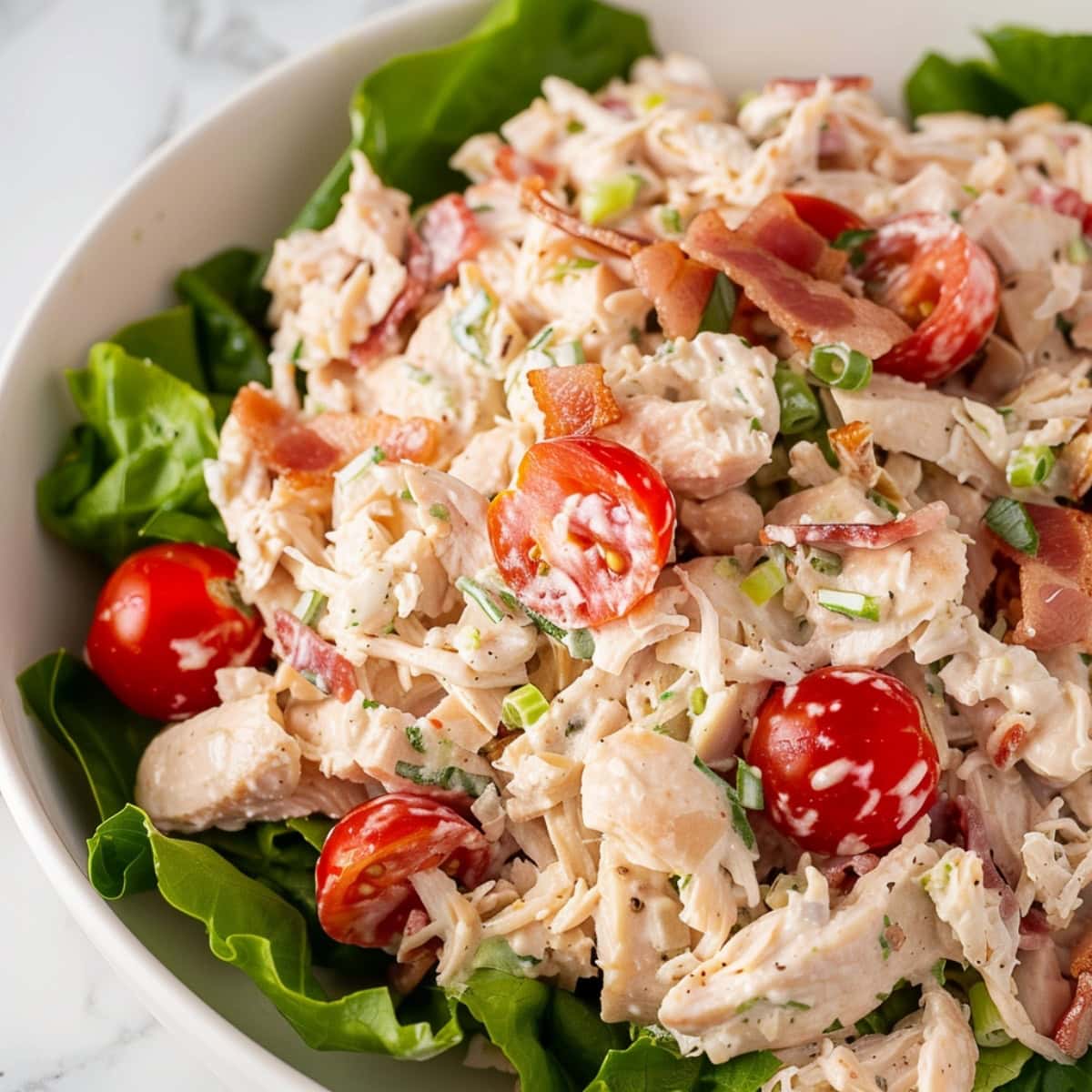 A plate of vibrant of BLT chicken salad in a bed of lettuce.