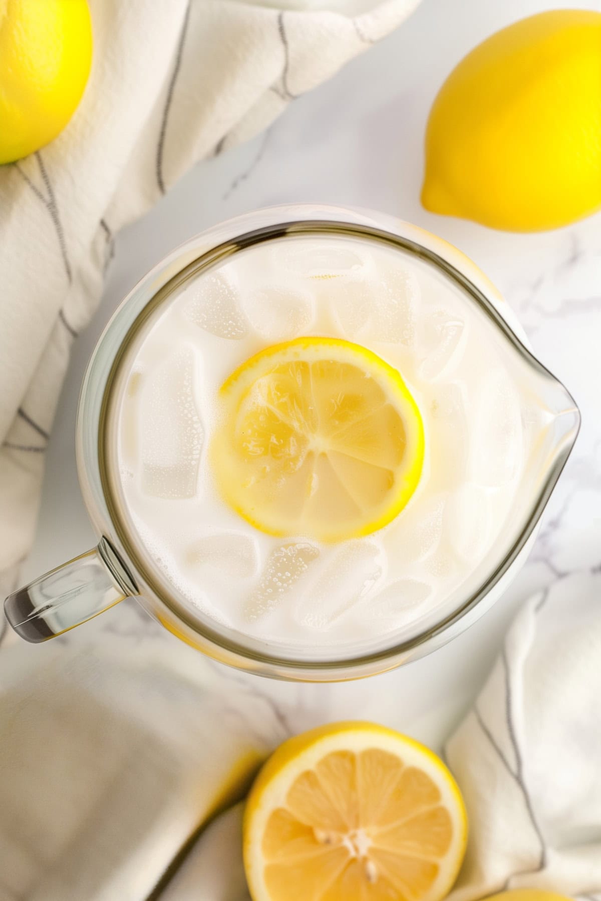 Rich and creamy lemonade in a glass pitcher with ice and fresh lemon slices, top view