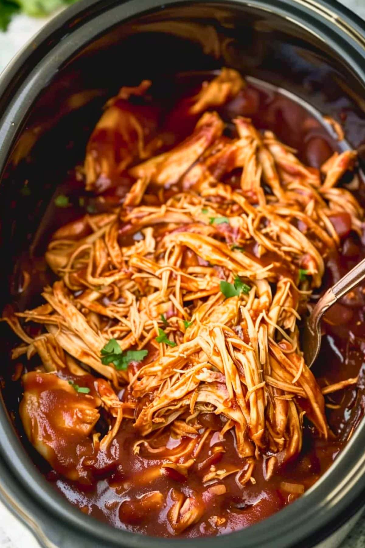 Shredded chicken in barbeque sauce inside a slow cooker.