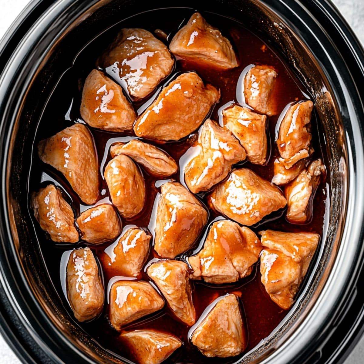 Bite sized chicken thigh with bourbon, soy sauce, brown sugar, ketchup, vinegar, honey, garlic, ginger, and red pepper flakes marinade cooked in a slow cooker. 