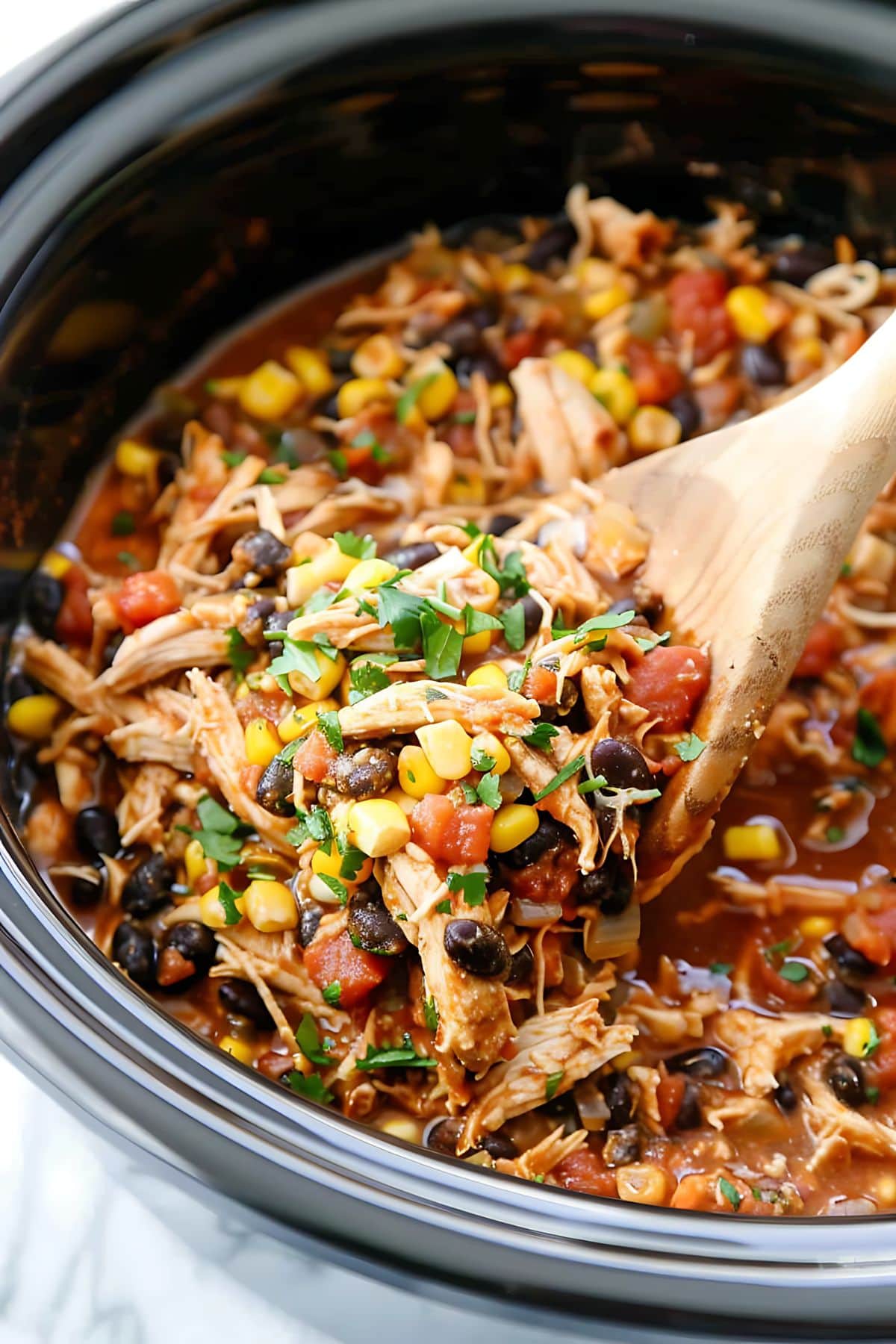 Chicken tacos in a Crockpot with a wooden ladle.