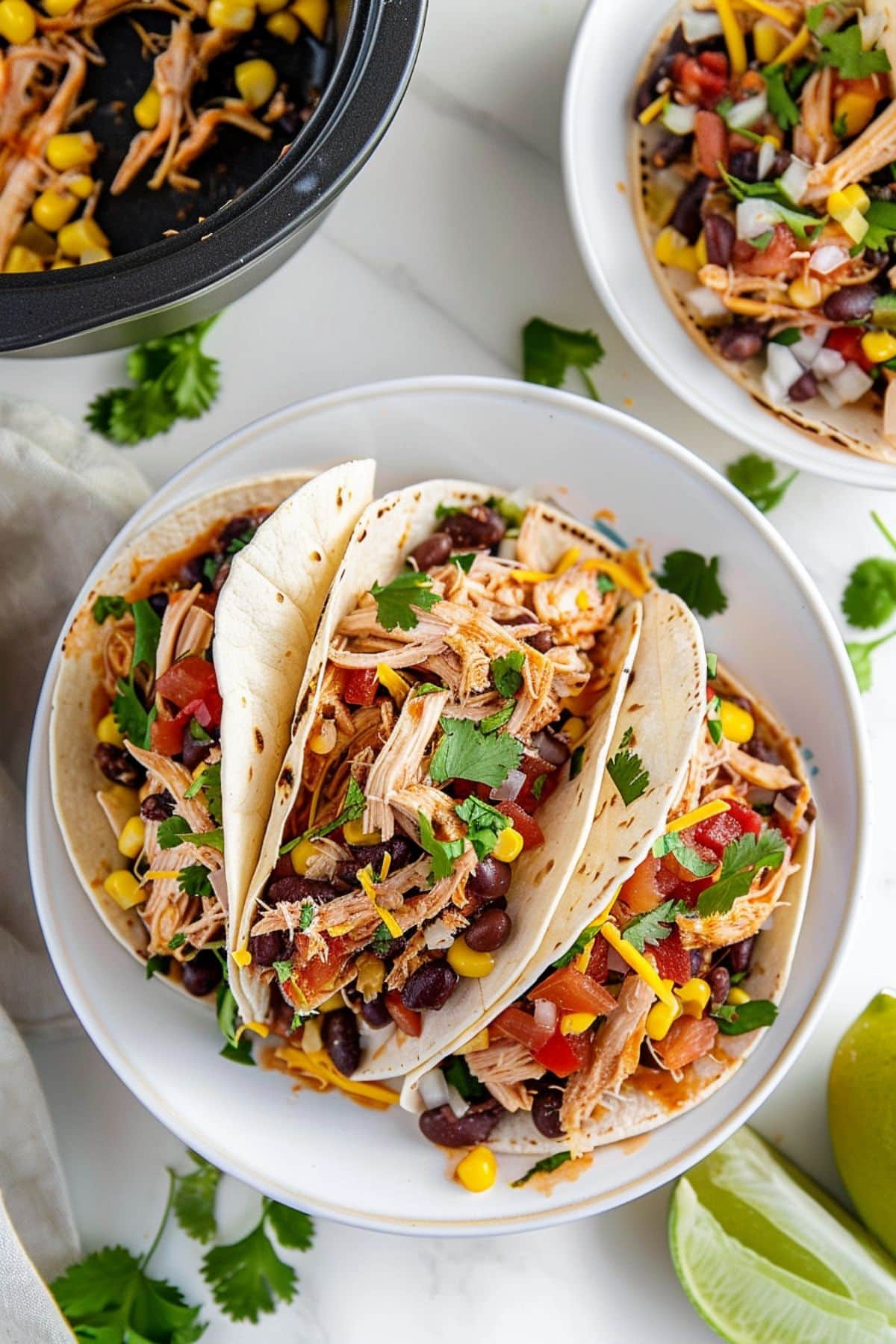 Taco shells with with shredded chicken, corn, black beans and salsa arranged on a white plate.