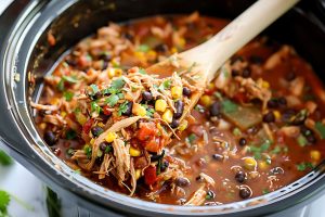 Shredded chicken in a Crockpot with wooden ladle.