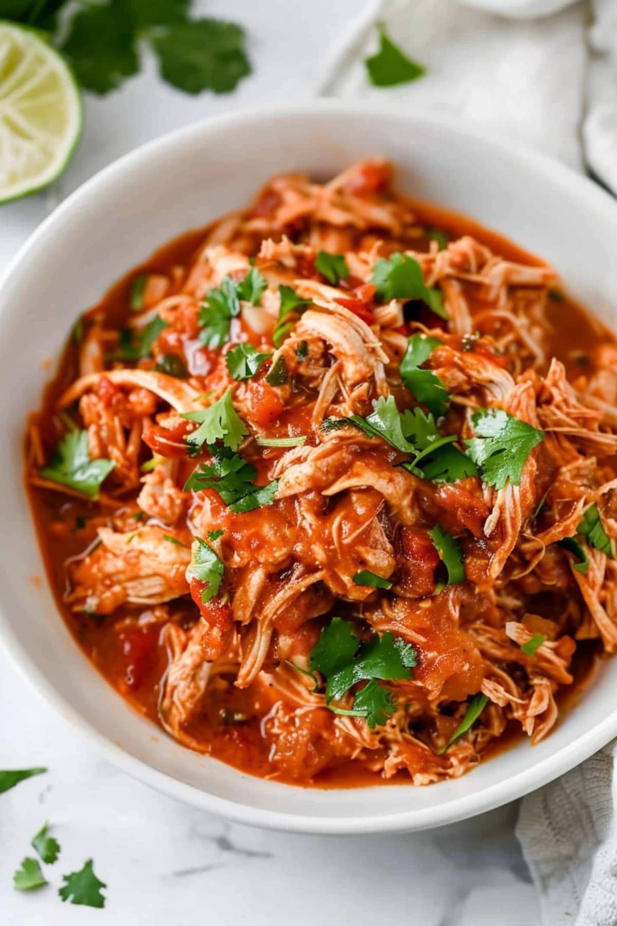 Tender and juicy homemade crockpot salsa chicken in a white bowl.