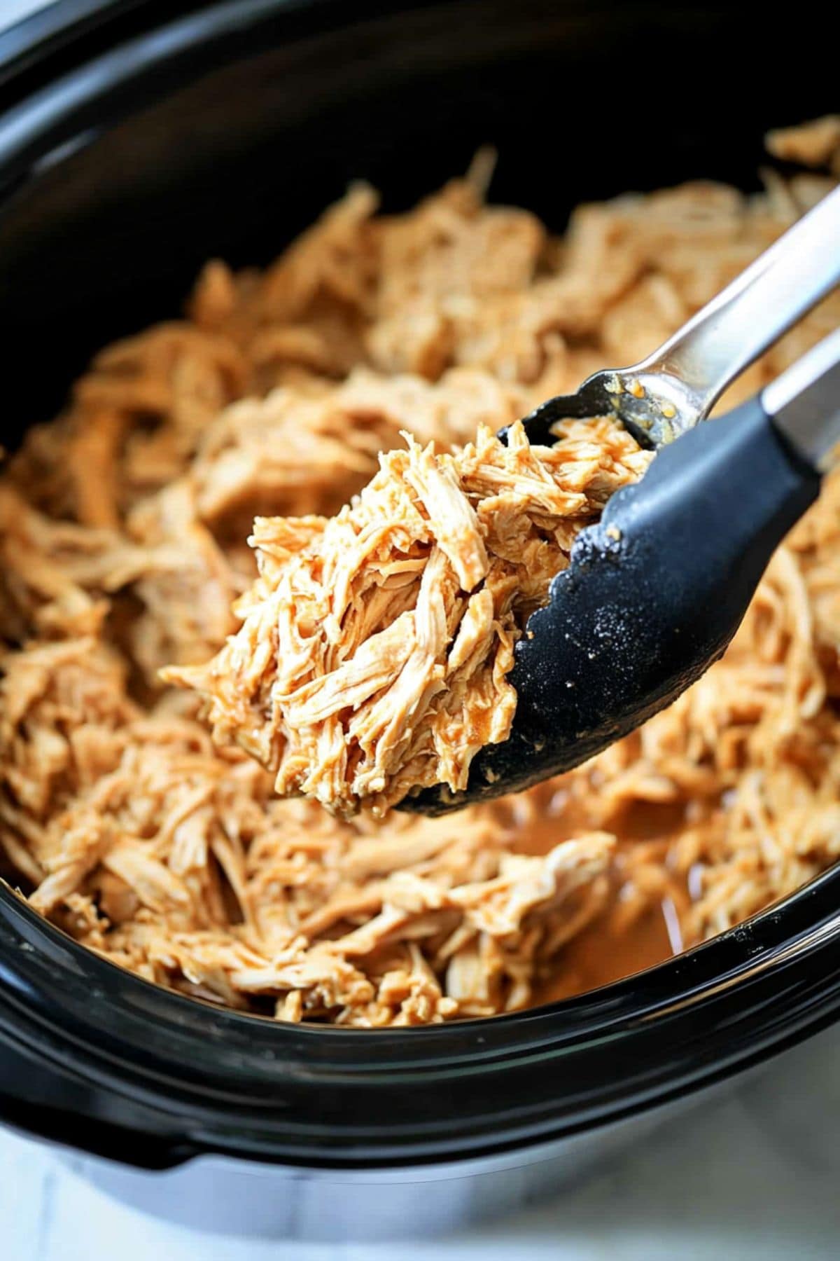 Tong with a serving of shredded chicken cooked inside a slow cooker crockpot.