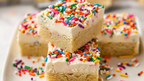 Frosted sugar cookie bars arranged on a square plate.