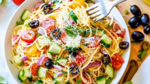 Spaghetti salad made with thin spaghetti broken into thirds, grated Parmesan cheese, seeded and chopped red bell pepper, thinly sliced red onion, halved cherry tomatoes, and mini pepperoni, sliced black olives served in a white plate, fork on the side.