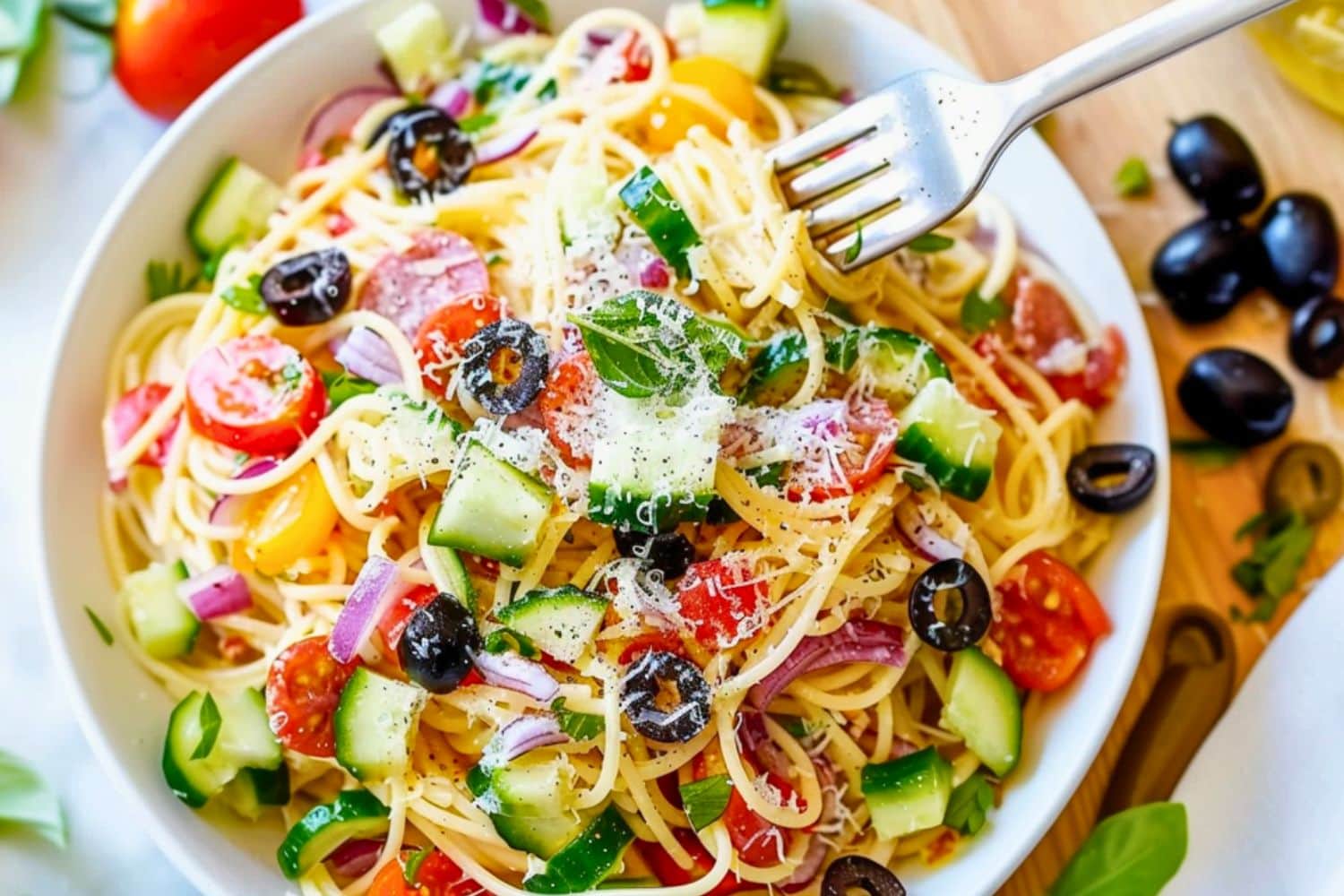 Spaghetti salad made with thin spaghetti broken into thirds, grated Parmesan cheese, seeded and chopped red bell pepper, thinly sliced red onion, halved cherry tomatoes, and mini pepperoni, sliced black olives served in a white plate, fork on the side.