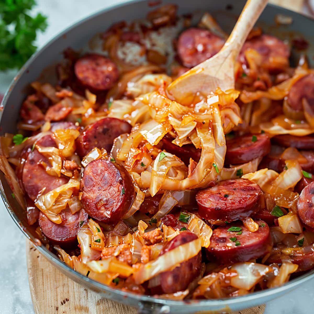 Wooden spoon scooping cabbage and sausage in skillet.