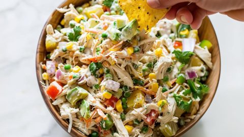 Tortilla dipped in a serving of Mexican chicken salad in a wooden bowl.