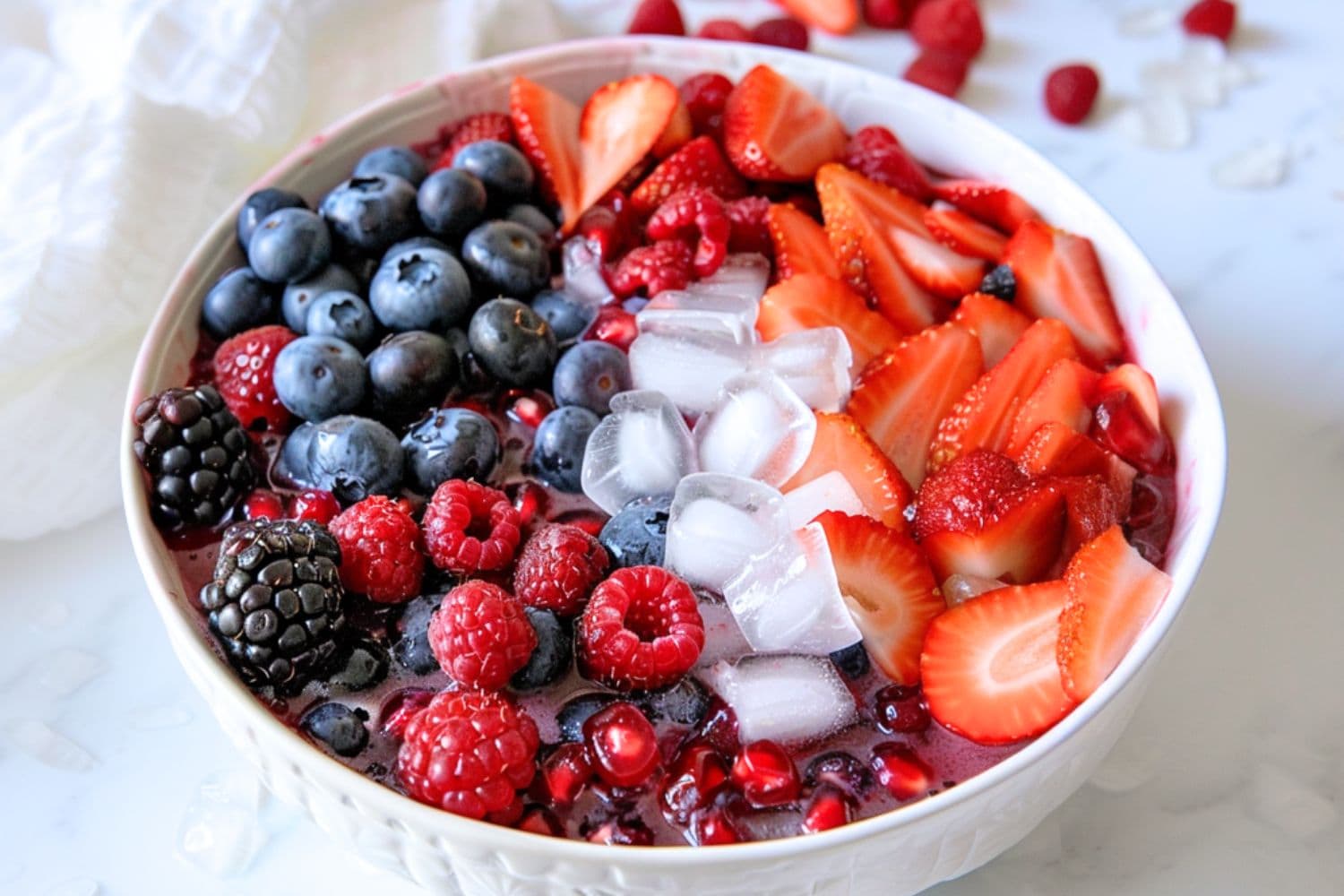 Mix of blueberries, blackberries, raspberries, pomegranate seeds, and chopped strawberries in a white bowl with cube ice and coconut water.