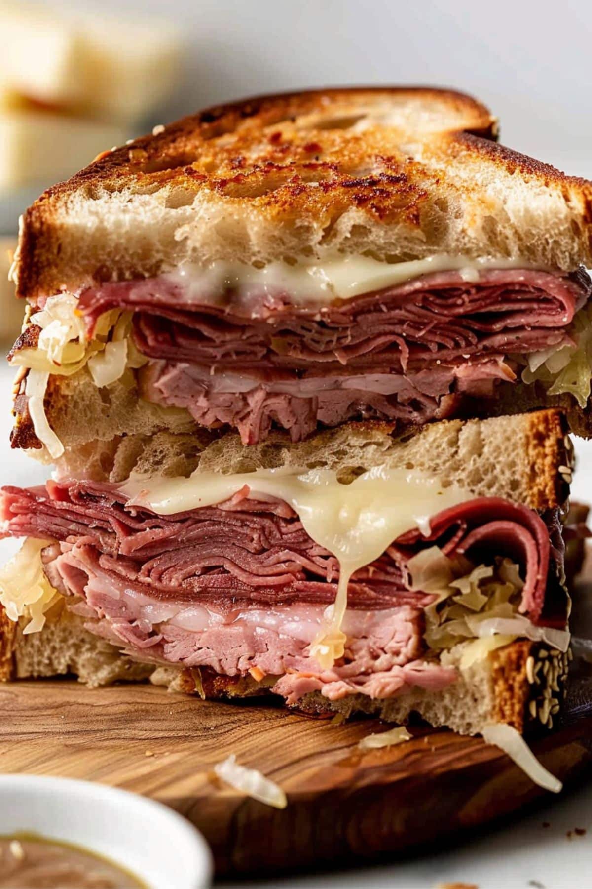 Pastrami sandwich sliced in half stack on top of each slices served on a wooden board.