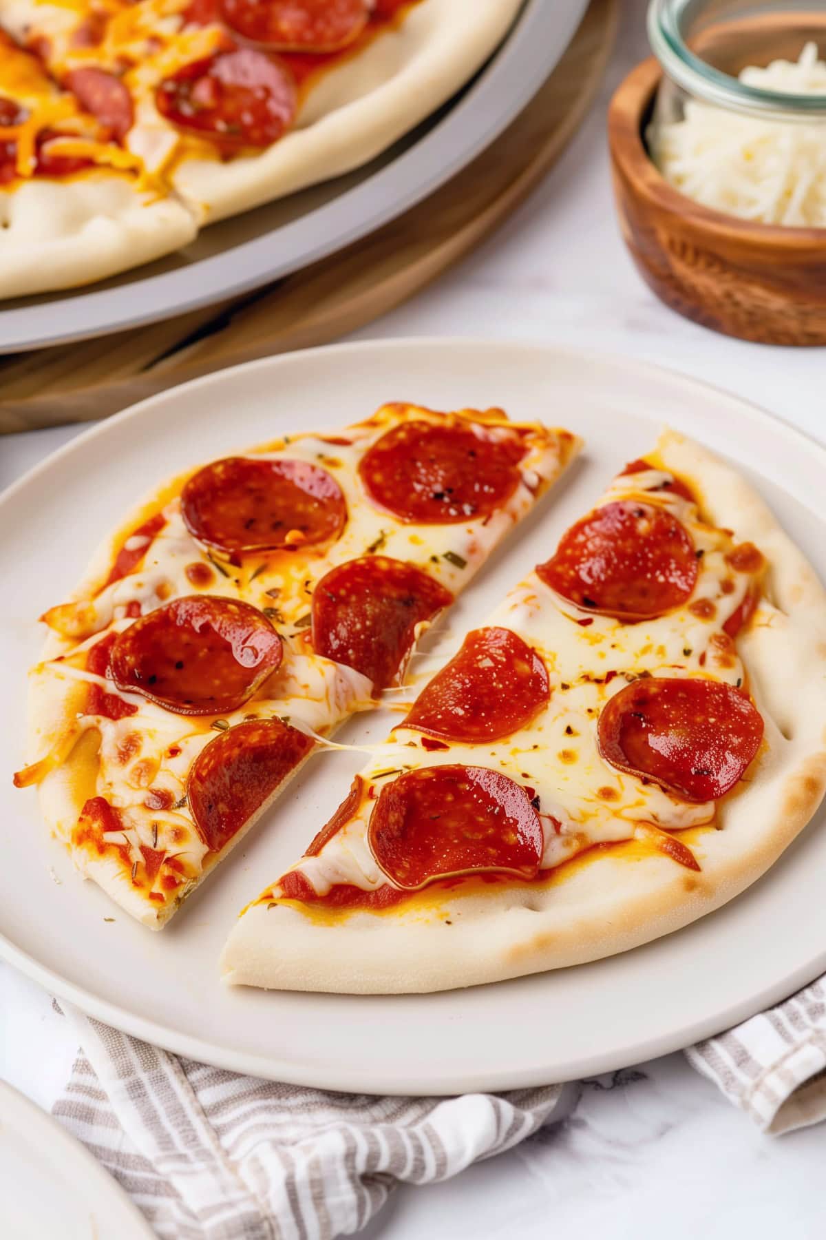 Cheesy homemade pita pizza topped pepperoni in a white plate.