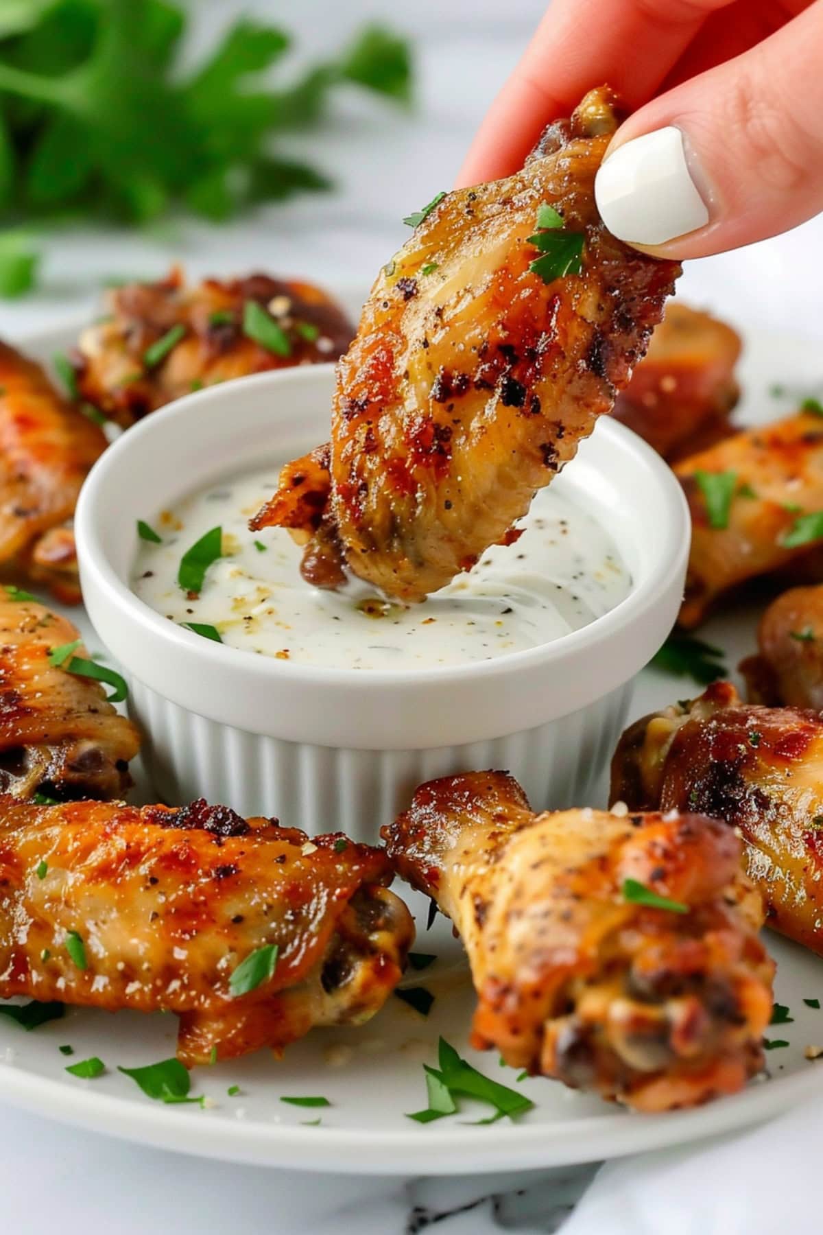 Hand holding a ranch chicken wing and dipping it to ranch dressing in a ramekin bowl.