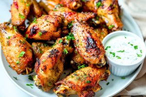 Baked ranch chicken wings in a white plate with ranch dressing on the side.